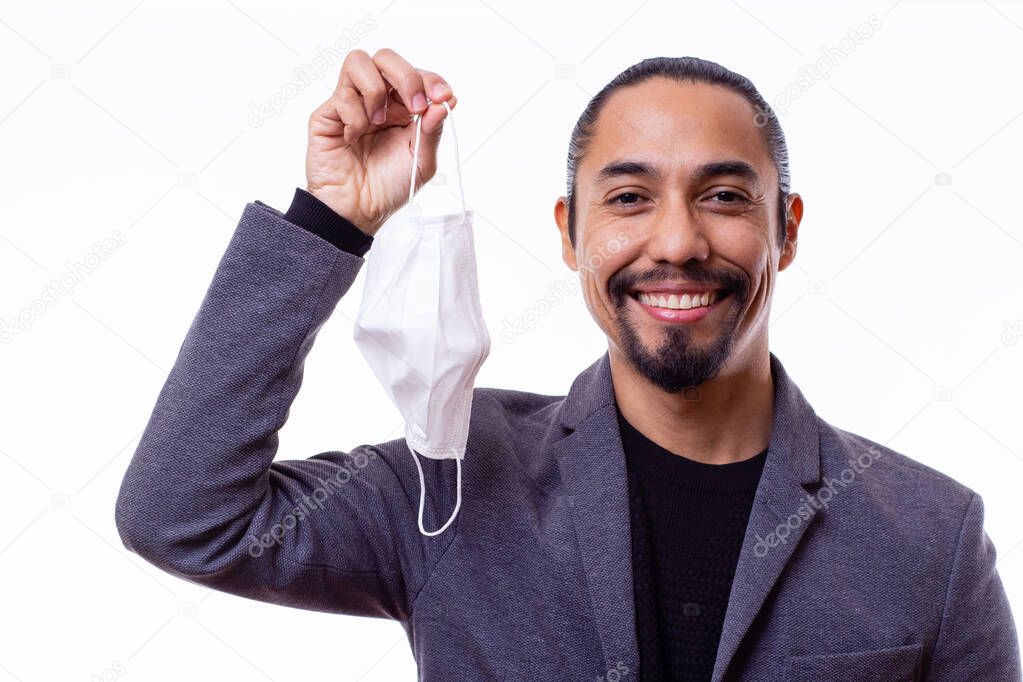 Portrait of a young Latino businessman ends his quarantine and smiles happily while holding his medical mask in one hand on a white background. Coronavirus concept.