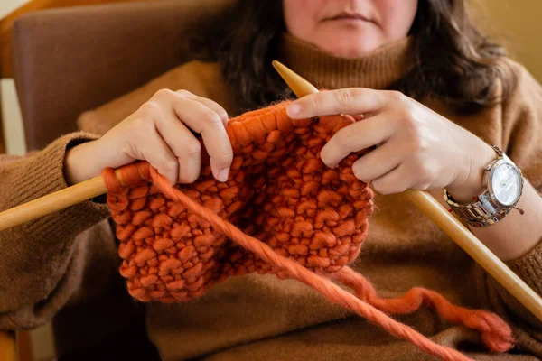 Woman knitting a cozy woolen garment sitting on her furniture at home. Work at home concept