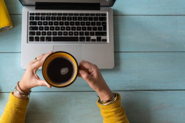 Evden ders çalışan bir kadının seçici odağı bir fincan kahve tutuyor. Ev eğitimi konsepti. Boşluğu kopyala