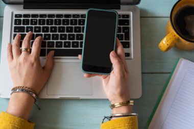 Dizüstü bilgisayarında yazı yazan ve akıllı telefonundan mesaj alan bir kadın. Ev konseptinde çalış.