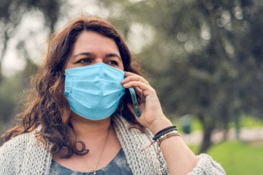 Kendini tıbbi bir maskeyle koruyan ve akıllı telefonuyla konuşan genç bir kadının portresi. Coronavirus konsepti. Boşluğu kopyala.
