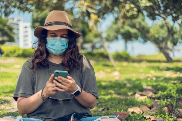 Cep telefonuna bakan şapkalı bir kadının portresi tıbbi bir maskeyle korunuyor ve açık havada. Yeni normal. Boşluğu kopyala