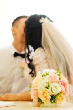 Blurry photo of the bride and her fiance on their wedding day. Bouquet in the foreground. clipart