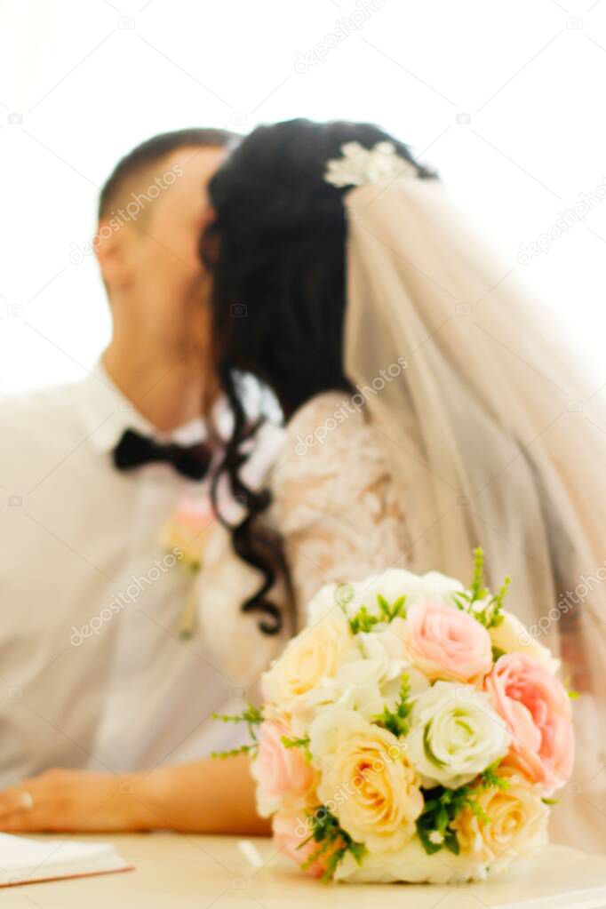 Blurry photo of the bride and her fiance on their wedding day. Bouquet in the foreground.