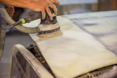 Araba tamirhanesinde araba cilalayan bir adamın elinde öğütücü..