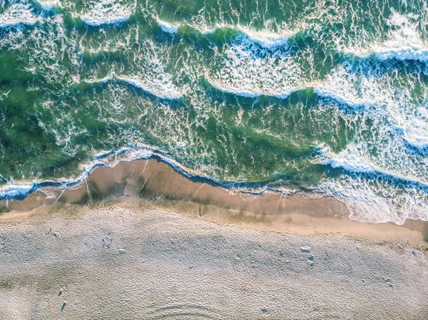 Aerial view of crashing wave in ocean with warm sunset light. Wave crashing on reef. Top view