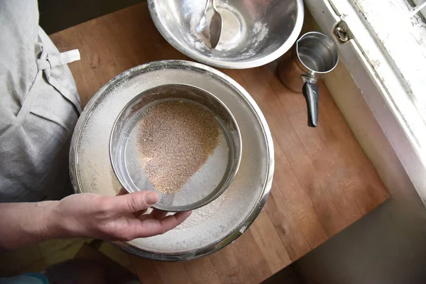 一个女厨师在围裙里把面粉筛入金属碗里 准备为烘焙制作面团 自制的松饼 高质量的照片 — 图库照片