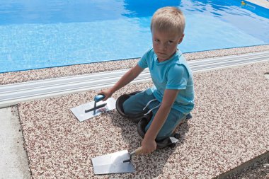 Küçük bir çocuk havuz etrafında yeni bir kaldırım üzerinde çalışıyor.