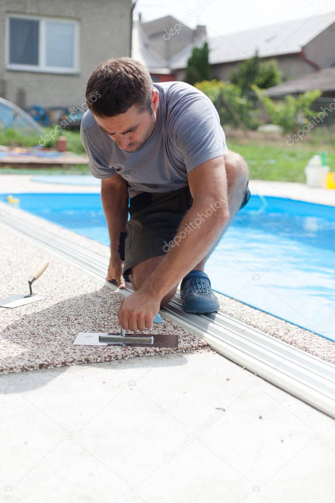 A little boy is working on a new pavement around the pool.