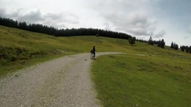 Avusturya Alpleri'nde yaz saati. Bisiklet eteklerinde genç bir kadın. Güzel bisikletçi güzel manzara ile sürmek. Avusturya Alp Bisiklet Yolu. Stabilize video.