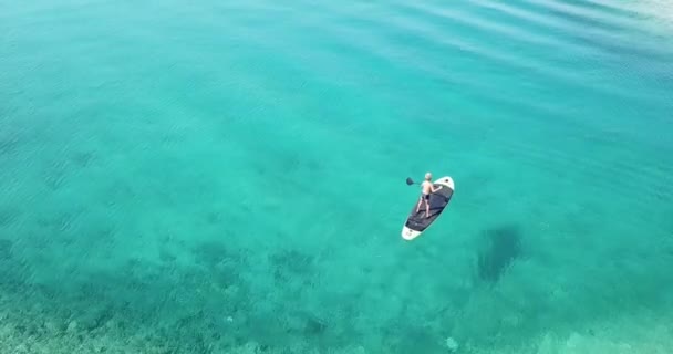 海のそばの夏時間 パドルボード上の子供の空中ビュー パドルボードでかわいい子供の学習 安定した4Kビデオ — ストック動画