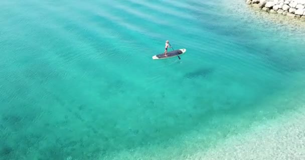 海のそばの夏時間 パドルボード上の子供の空中ビュー パドルボードでかわいい子供の学習 安定した4Kビデオ — ストック動画