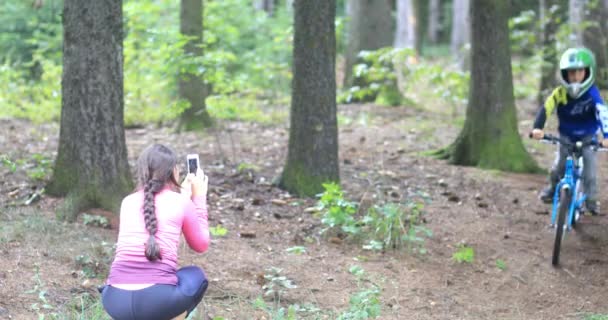 森の中で難しいトラックに乗っている小さな男の子 彼の母親は彼の携帯電話で彼を撃つ — ストック動画