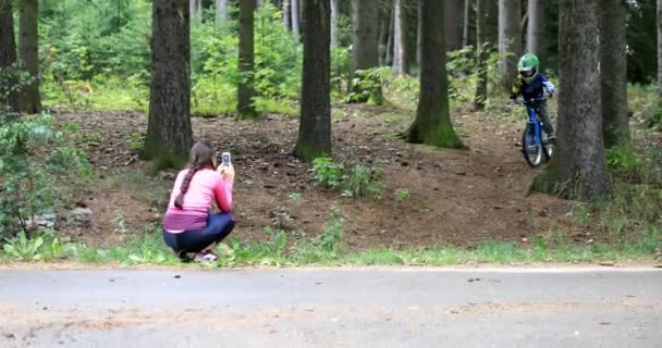 森の中で難しいトラックに乗っている小さな男の子 彼の母親は彼の携帯電話で彼を撃つ — ストック動画