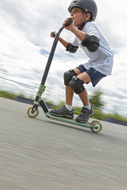 Küçük tatlı bir çocuk kaykay parkında scooter sürüyor. Genç bir acemi sporcu ekstrem sporlarda boş zaman geçirir. Hareket fotoğrafı, değiştirilebilir hareket bulanıklığı.