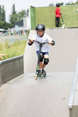 Küçük tatlı bir çocuk kaykay parkında scooter sürüyor. Genç bir acemi sporcu ekstrem sporlarda boş zaman geçirir. Yaşam biçimi.