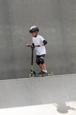 Küçük tatlı bir çocuk kaykay parkında scooter sürüyor. Genç bir acemi sporcu ekstrem sporlarda boş zaman geçirir. Yaşam biçimi.