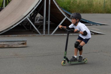 Küçük tatlı bir çocuk kaykay parkında scooter sürüyor. Genç bir acemi sporcu ekstrem sporlarda boş zaman geçirir. Yaşam biçimi.