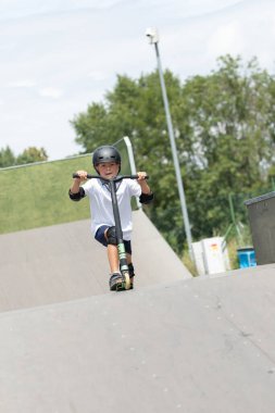 Küçük tatlı bir çocuk kaykay parkında scooter sürüyor. Genç bir acemi sporcu ekstrem sporlarda boş zaman geçirir. Yaşam biçimi.