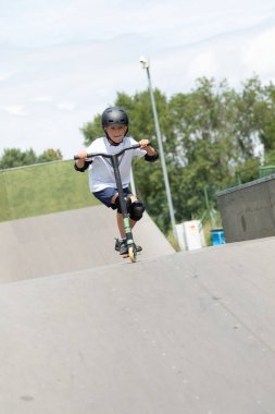 Küçük tatlı bir çocuk kaykay parkında scooter sürüyor. Genç bir acemi sporcu ekstrem sporlarda boş zaman geçirir. Yaşam biçimi.