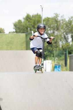 Küçük tatlı bir çocuk kaykay parkında scooter sürüyor. Genç bir acemi sporcu ekstrem sporlarda boş zaman geçirir. Yaşam biçimi.