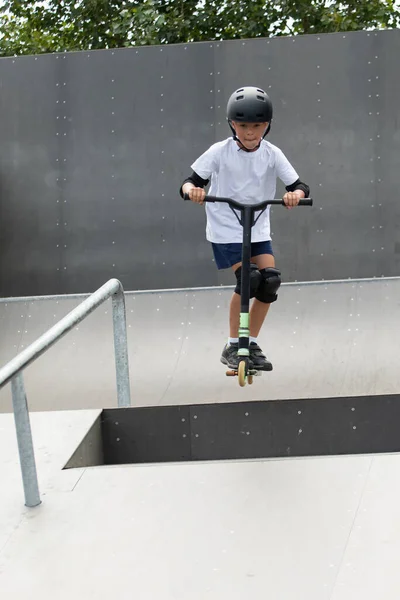 かわいい男の子がスケートパークでスクーターに乗っています 若い初心者の選手は極端なスポーツで自由な時間を過ごす ライフスタイル — ストック写真