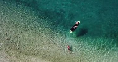Deniz kenarında yaz zamanı. Kürek tahtasında çocuğun havadan görünüşü. Kürek tahtasında öğrenen sevimli bir çocuk. 4K videosu sabitlendi.