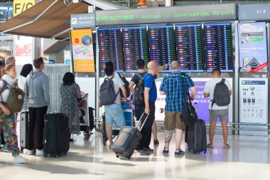 Bangkok, Tayland - 13 Ekim 2019: Uluslararası Havalimanı Suvarnabhumi çalışanları uçuş takvimi ekranına, pano yakınındaki yolculara, uçak kalkış veya varış zamanı ve geçit bilgilerine bakıyorlar 