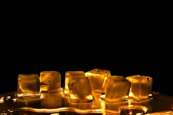 黒の背景に黄金の氷のキューブを隔離された閉鎖 透明な凍結融解琥珀色の水 黄色のバックライト 抽象的な冷たいアルコール飲料のコンセプト 夜のパーティーのデザイン コピースペース — ストック写真