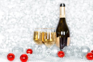 İki kadeh şampanya ve bir şişe şampanya, yeni yılın kırmızı ve beyaz topları, gümüş süsleme arkaplanı bulanık bokeh arkaplan, Noel ve yeni yıl tebrik kartı, poster, afiş
