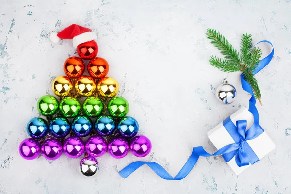 Parlak süslemelerden yapılmış Noel ağacı LGBT topluluk gökkuşağı renkleri, Noel Baba şapkası, hediye kutusu, mavi kurdele, çam dalı, LGBTQ gurur sembolü, yeni yıl tebrik kartı şablonu, kopyalama alanı