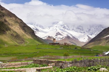 Yeşil vadi ve dağların tepelerindeki antik kule kar ve bulutlarla kaplı arka plan, Georgia