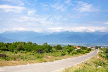 Kırsalda boş bir yol ufukta dağlar ve bulutlu mavi bir gökyüzü.