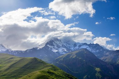 Kar ve yeşil tepelerdeki manzara dağ zirveleri, derin mavi gökyüzü ve büyük beyaz bulutlar arka plan, Kafkas dağları, Kazbek dağı, Gürcistan