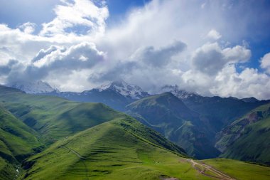 Kar ve yeşil tepelerdeki manzara dağ manzaraları, derin mavi gökyüzü ve büyük beyaz bulutlar arka plan, Kafkas dağları, Kazbek dağı, Gürcistan