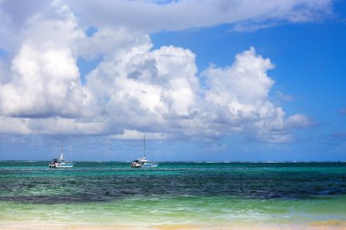 Gök mavisi denizde iki tekne, Karayip plajı, mavi gökyüzü ve büyük beyaz bulutlar.