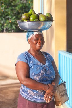 Bayahibe, Dominik Cumhuriyeti, 31 Aralık 2016, Kafasında kase olan gülümseyen yeşil avokadolarla Afrikalı kadın