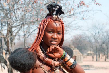 Otjikandero Himba Köyü, Namibya - 8 Eylül 2017: Geleneksel himba köyü geçmişinde ulusal saç stili, yüzük, kolye ve bileziklere sahip güzel himba kızı