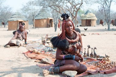 Otjikandero Himba Yetimhanesi Köyü, Namibya - 8 Eylül 2017: Himba kızı geleneksel köy pazarında hediyelik eşya, kilden evler satıyor