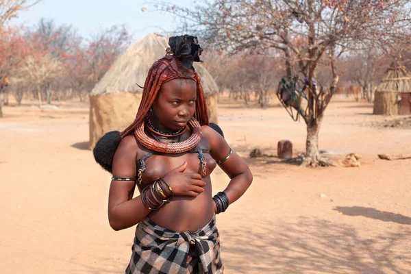 Otjikandero Himba Yetimhanesi Köyü, Namibya - 8 Eylül 2017: Geleneksel köyde genç Himba kadını, kilden evler
