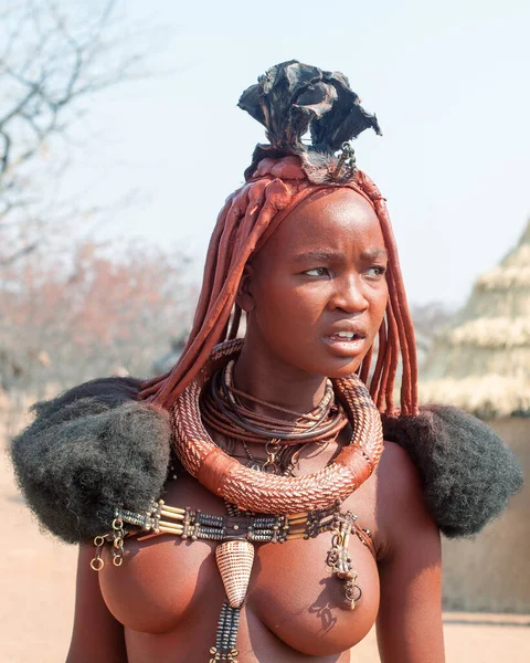Otjikandero Himba Köyü, Namibya - 8 Eylül 2017: Himba Çamurlu kil evlerde geleneksel saç stiline, yüzüklere ve kolyeye sahip güzel Himba kadını