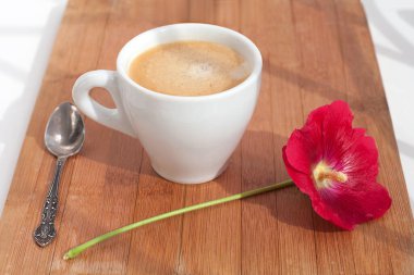Mallow kırmızı çiçek dalı ve ahşap arka planda gümüş kaşıklı köpüklü beyaz kahve fincanı.