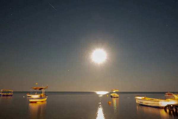 Ay ışığında deniz manzarası ve tekneler