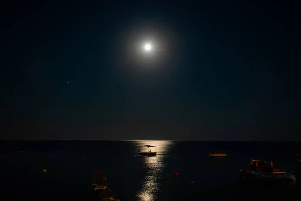 Ay ışığında deniz manzarası ve tekneler