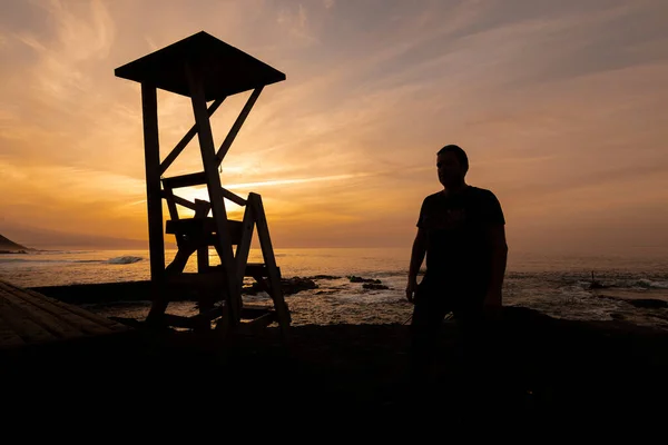 Gün batımında sahilde ışıklandırılmış biri.