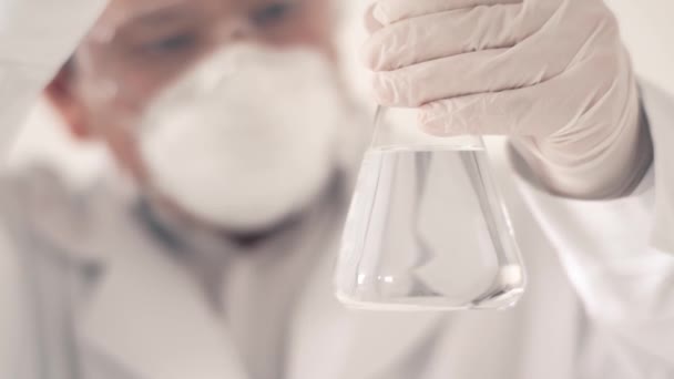 Chemik lub naukowiec w laboratorium trzyma probówkę z substancją chemiczną w ręku. Przeprowadzi eksperyment wlewając płyn do kolby. Badanie — Wideo stockowe