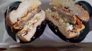 Biftekli iki dilim lezzetli hamburger, erimiş peynir, marul ve sebze. Mutfakta malzemelerle hazırlanmış iki yarım hamburger.