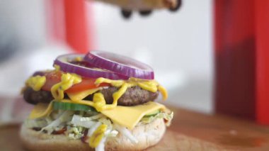 Şefler siyah lastik eldivenlerle topuzun ikinci kısmını alıyor ve hamburgere basıyor. Lezzetli yemek. Mutfak masasında leziz bir hamburger.