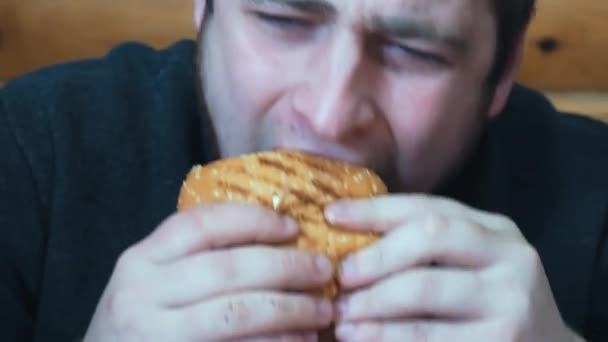 Uma pessoa prova a deliciosa carne de um hambúrguer grande com queijo e vegetáveis.Obtém prazer de um delicioso hambúrguer — Vídeo de Stock