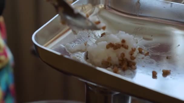Een vrouw voegt een eetlepel gehakt aan het vlees grinder.cooking een schotel rijst en boekweit met een elektrisch vlees grinder.processing van gekookte granen door malen in de keuken — Stockvideo